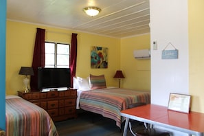 Une chambre avec deux lits, une télévision, une commode, une table et un tableau au mur.