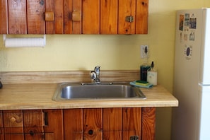 Una cocina con armarios de madera, un lavamanos de acero inoxidable y un refrigerador.