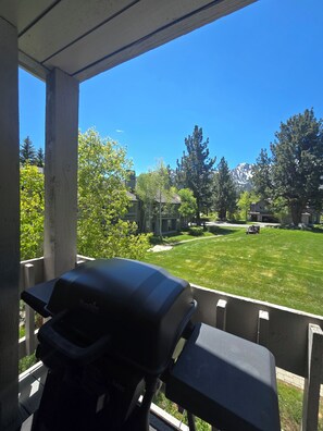 Un patio con una parrilla, vista a un césped verde y casas al fondo.