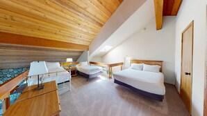 Een slaapkamer met twee bedden, een houten plafond, een klein tafeltje en een nachtkastje met een lamp.