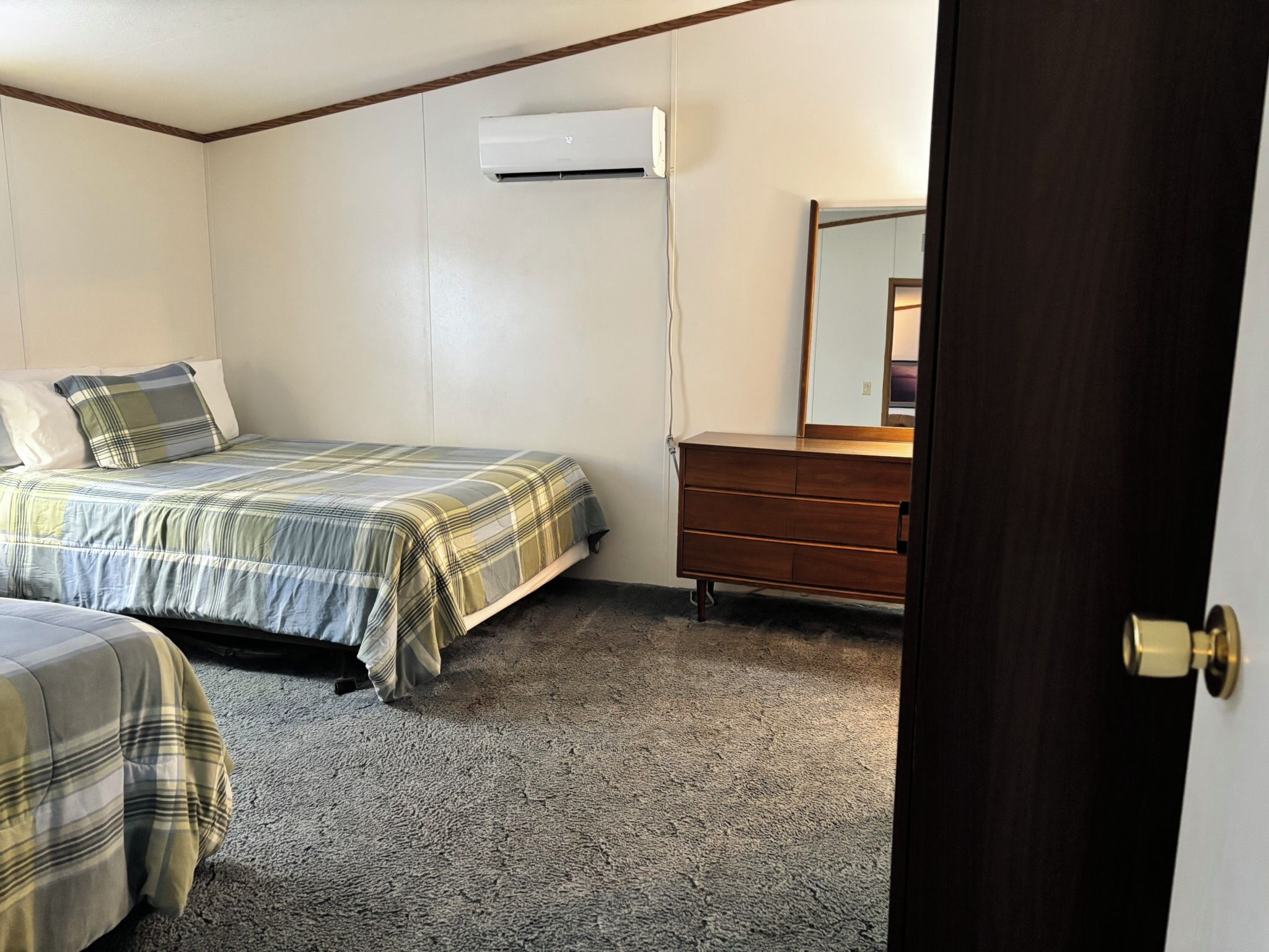 A bedroom with two beds, a dresser, a mirror, and an air conditioning unit.