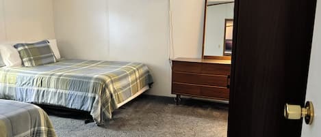 A bedroom with two beds, a dresser, a mirror, and an air conditioning unit.