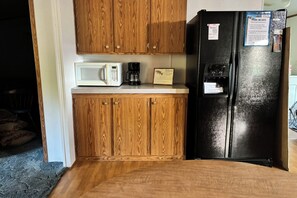 A compact kitchen with wooden cabinets, a white microwave, a coffee maker, and a black refrigerator with a water dispenser.
