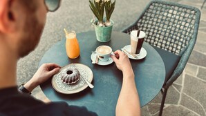 Una persona sentada a una mesa redonda con un postre, una bebida y una taza de café.