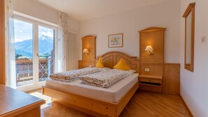 Un dormitorio con cama de madera, dos mesitas de noche con lámparas, una ventana con vistas a montañas y un armario de madera.
