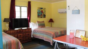 A room with two beds, a TV, a desk with a pitcher of water, and a welcome sign.