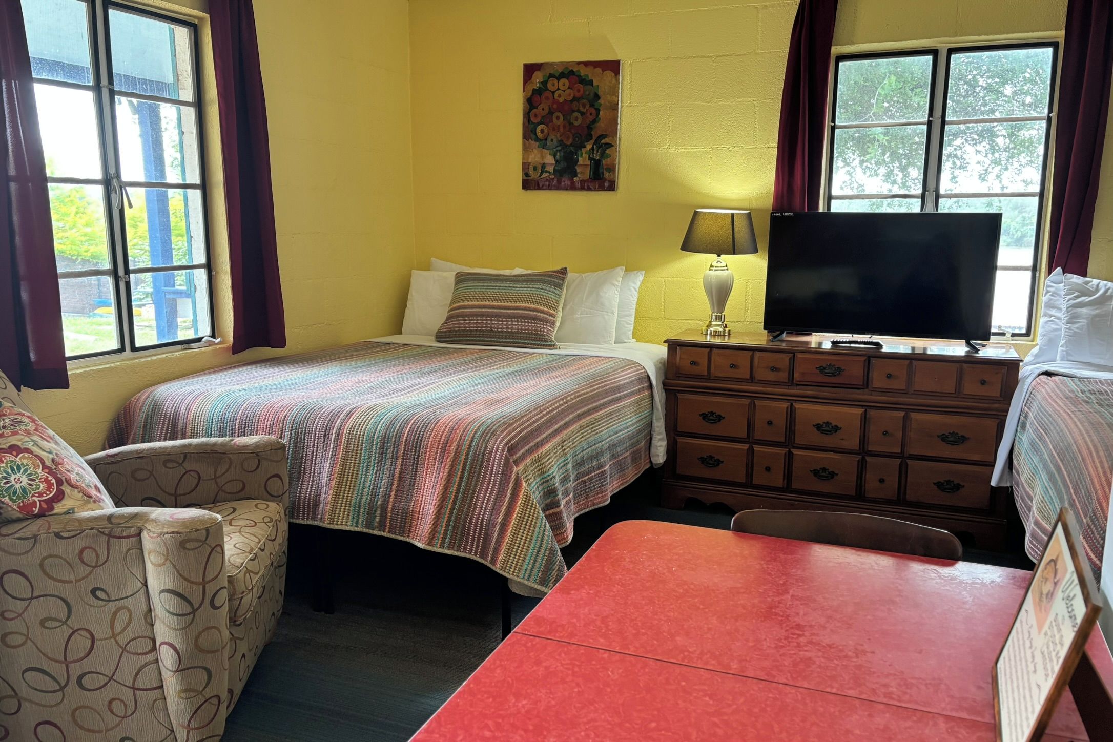 A room with a bed, a dresser, a television, and a painting on the wall.