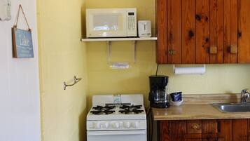 Uma cozinha com fogão branco, micro-ondas em uma prateleira, armários de madeira e cafeteira.