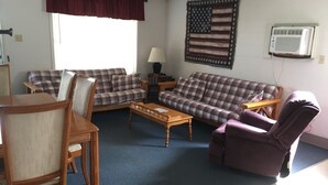 A living room with two plaid sofas, a wooden coffee table, a purple armchair, and a dining table with chairs.