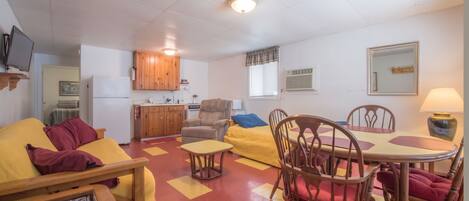 A compact living space with a kitchenette, a dining area with a table and chairs, a sofa, and a television mounted on the wall.
