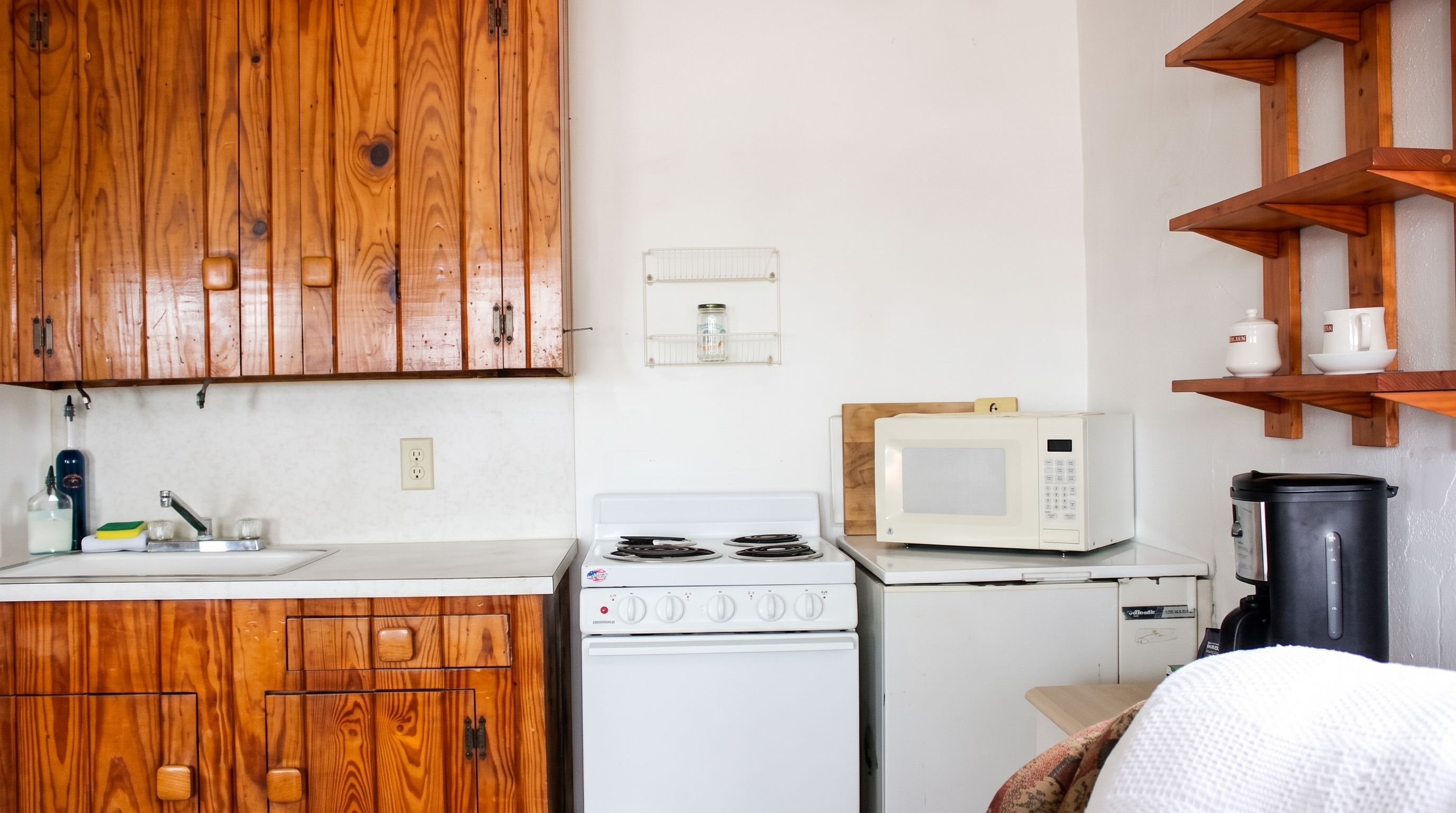 A compact kitchen with wooden cabinets, a white stove, a microwave, and a small refrigerator.