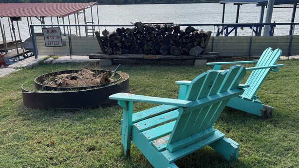A lakeside deck with a fire pit, stacked firewood, and two turquoise Adirondack chairs. - Studio #21-Efficiency (Kingsland)