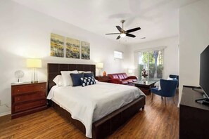 Un dormitorio con una cama grande, un escritorio, una silla, un sofá rojo y un ventilador de techo.