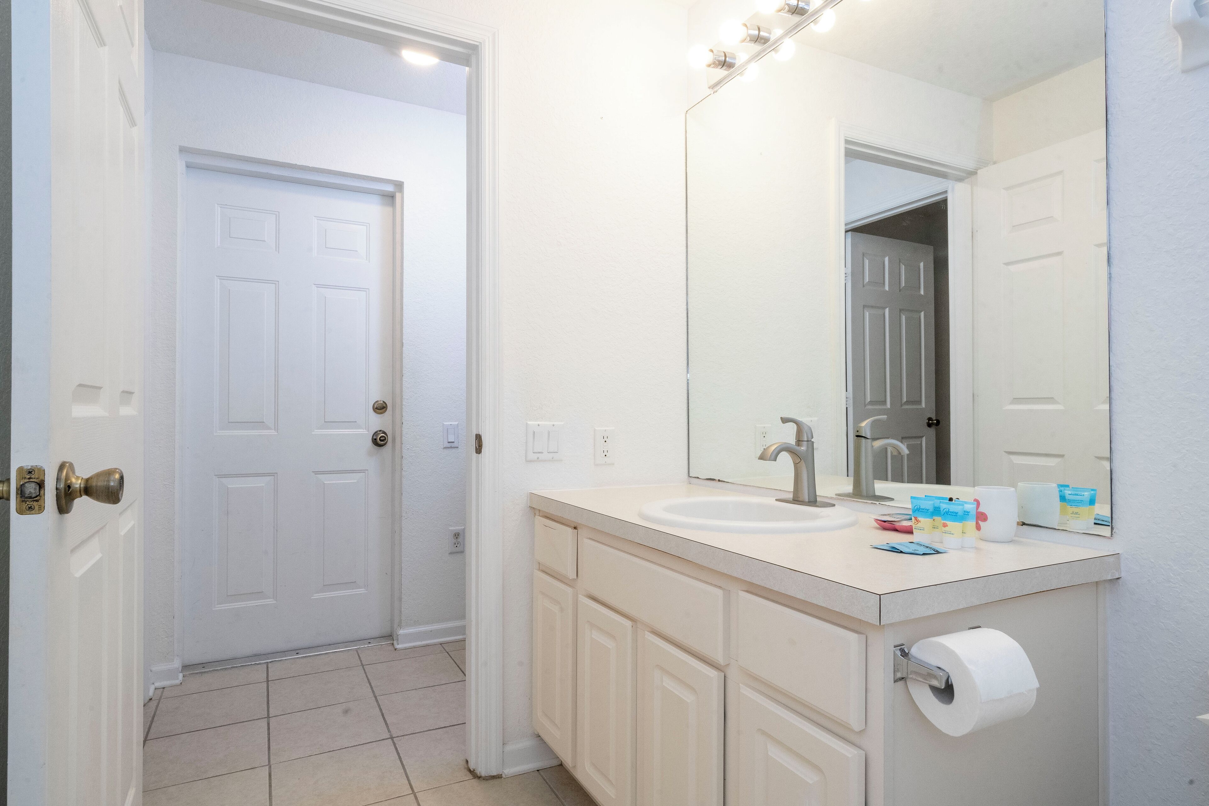 Une salle de bain avec une porte blanche, un lavabo avec un miroir et un porte-rouleau de papier toilette.