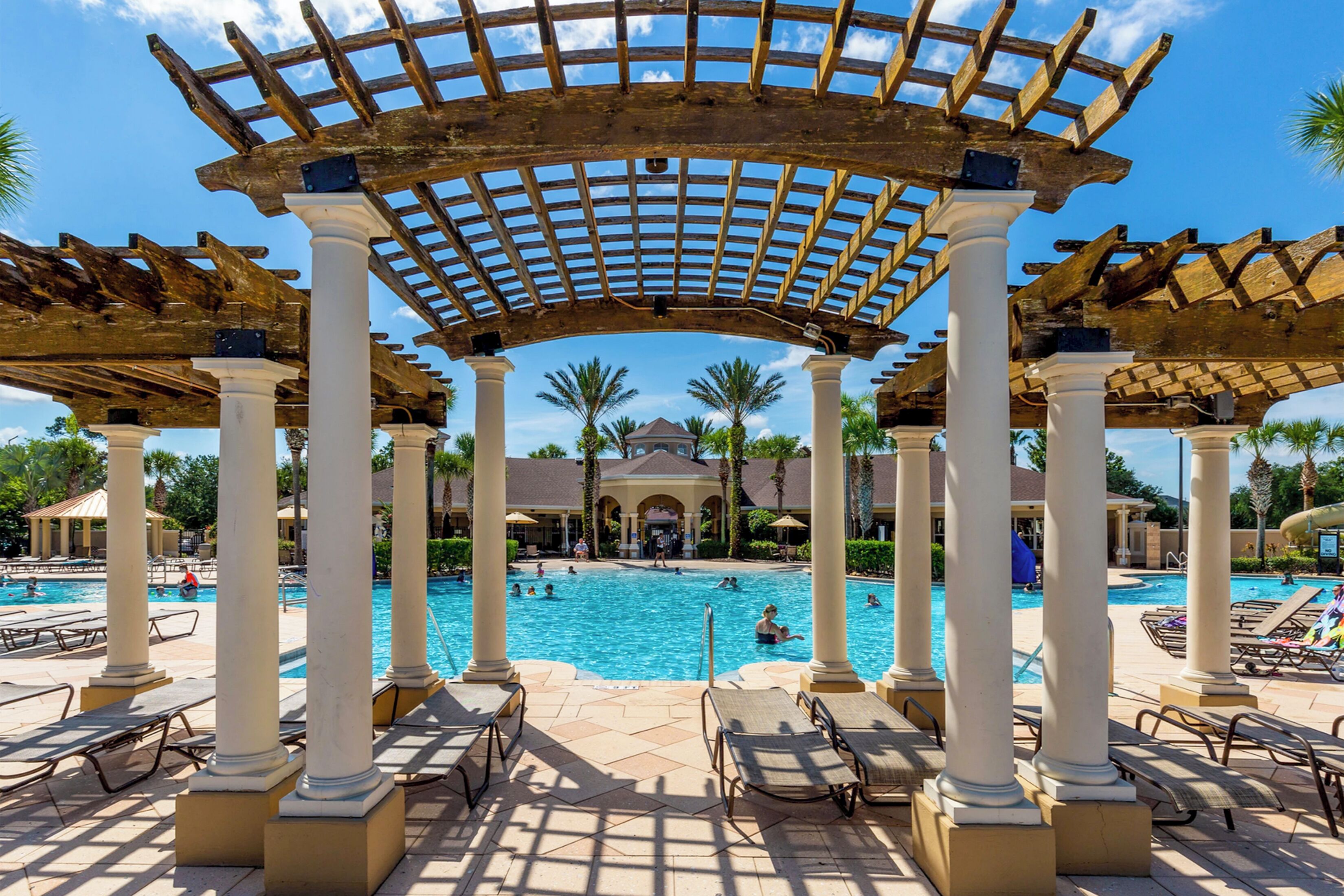 Un área de piscina con una estructura de pérgola, sillones de descanso y una vista despejada de la piscina.