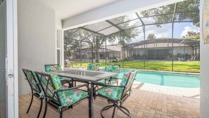 A covered patio with a pool, outdoor seating, and a view of a building in the background. - Your Dream Family Vacation Home – 5BR, 5BA & Sun-Filled South-Facing Pool! (Kissimmee)