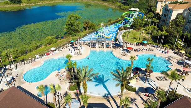 A large outdoor swimming pool with multiple lanes, surrounded by palm trees and lounge chairs. - Your Dream Family Vacation Home – 5BR, 5BA & Sun-Filled South-Facing Pool! (Kissimmee)