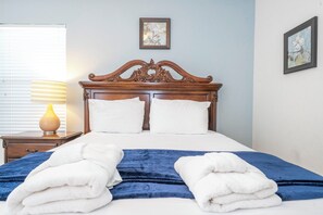 Un lit bien fait, recouvert d’une couverture bleue et blanche, avec une tête de lit en bois et deux oreillers.