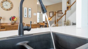 A kitchen with a modern faucet, wooden dining table, and a staircase in the background. - Your Dream Family Vacation Home – 5BR, 5BA & Sun-Filled South-Facing Pool! (Kissimmee)