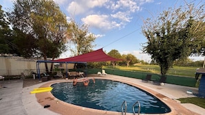 An outdoor swimming pool with a red canopy, surrounded by lounge chairs and a covered seating area. - Valentine Lakeside-Studio Cabin 2 (Kingsland)