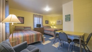 A room with two beds, a desk, and a chair. There is a lamp, a television, and a sign on the wall.