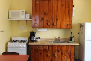 A compact kitchen with wooden cabinets, a microwave, a stove, a sink, and a refrigerator.