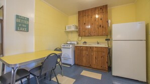A compact kitchen with a yellow table, a stove, a microwave, wooden cabinets, and a refrigerator.