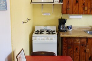 A compact kitchen with a white stove, wooden cabinets, a coffee maker, and a small sink. - Winter Texan Pet Friendly Cabin with Pool and WiFi (Kingsland)