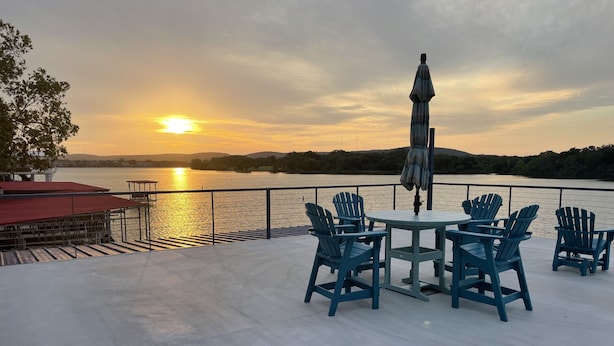 A deck with a table and chairs overlooking a lake at sunset.