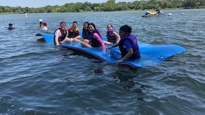 A group of people on a blue raft in a lake surrounded by greenery.