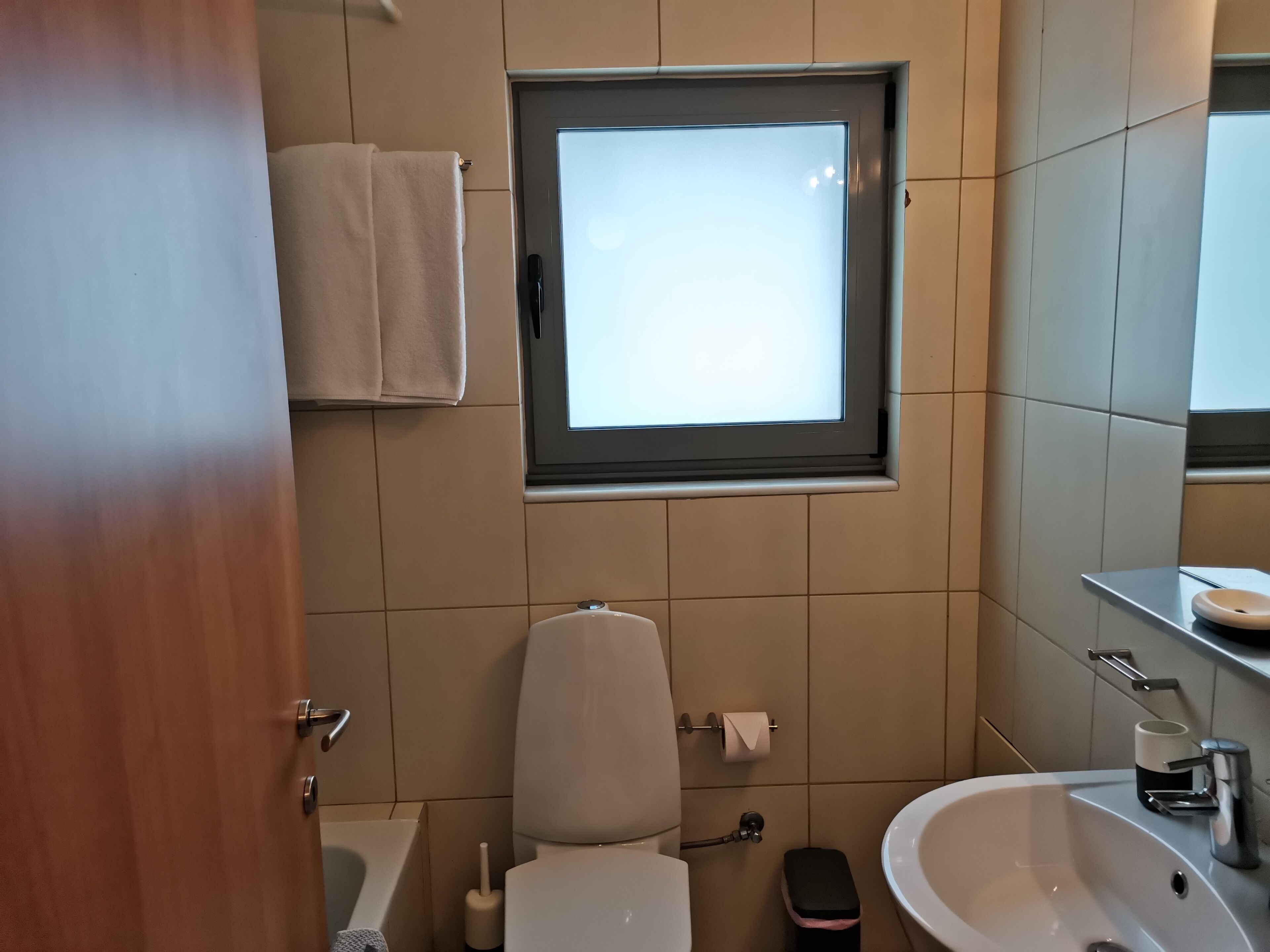 Ein modernes Badezimmer mit Toilette, Bidet, Waschbecken und einem Fenster über der Toilette.