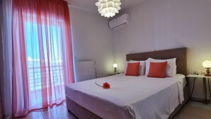 A hotel room with a large bed, a bedside table with a lamp, a window with sheer curtains, and a modern ceiling light fixture. - Domus Aries (Rethymno)