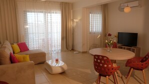 A living room with a sofa, a coffee table, a dining table with chairs, a TV, and a vase with flowers. - Domus Aries (Rethymno)