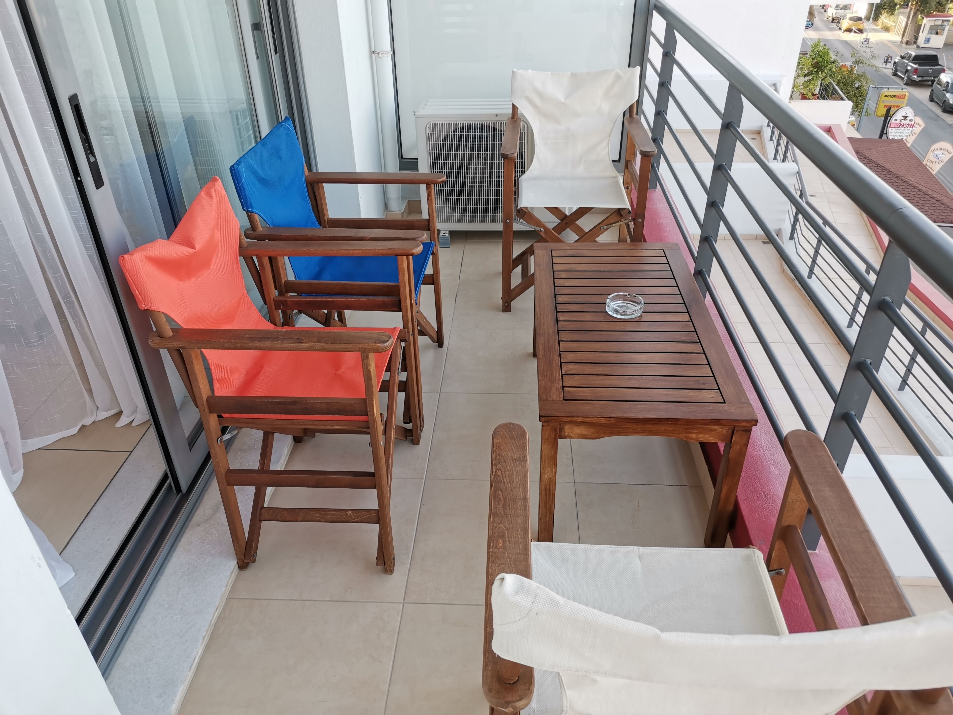 A balcony with wooden furniture, including chairs and a table, and a view of the street below.
