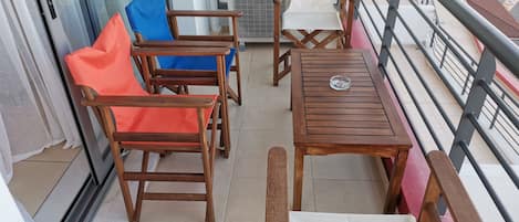 A balcony with wooden furniture, including chairs and a table, and a view of the street below.