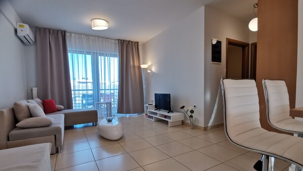 A modern living room with a sofa, ottoman, TV, and chairs. - Domus Aries (Rethymno)