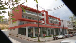 A modern building with a red and white facade, multiple balconies, and a ground-level entrance with glass doors. - Domus Aries (Rethymno)