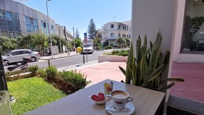 A table with a cup of coffee and a bowl of strawberries, overlooking a street with cars and buildings. - Domus Aries (Rethymno)
