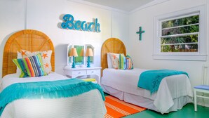 Un dormitorio con dos camas, una ventana con vistas a la vegetación, una cruz en la pared y un cartel que dice 'Beach'.