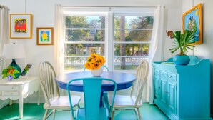 Una habitación con una mesa redonda, cuatro sillas, un jarrón con girasoles, un armario azul y dos cuadros en la pared.