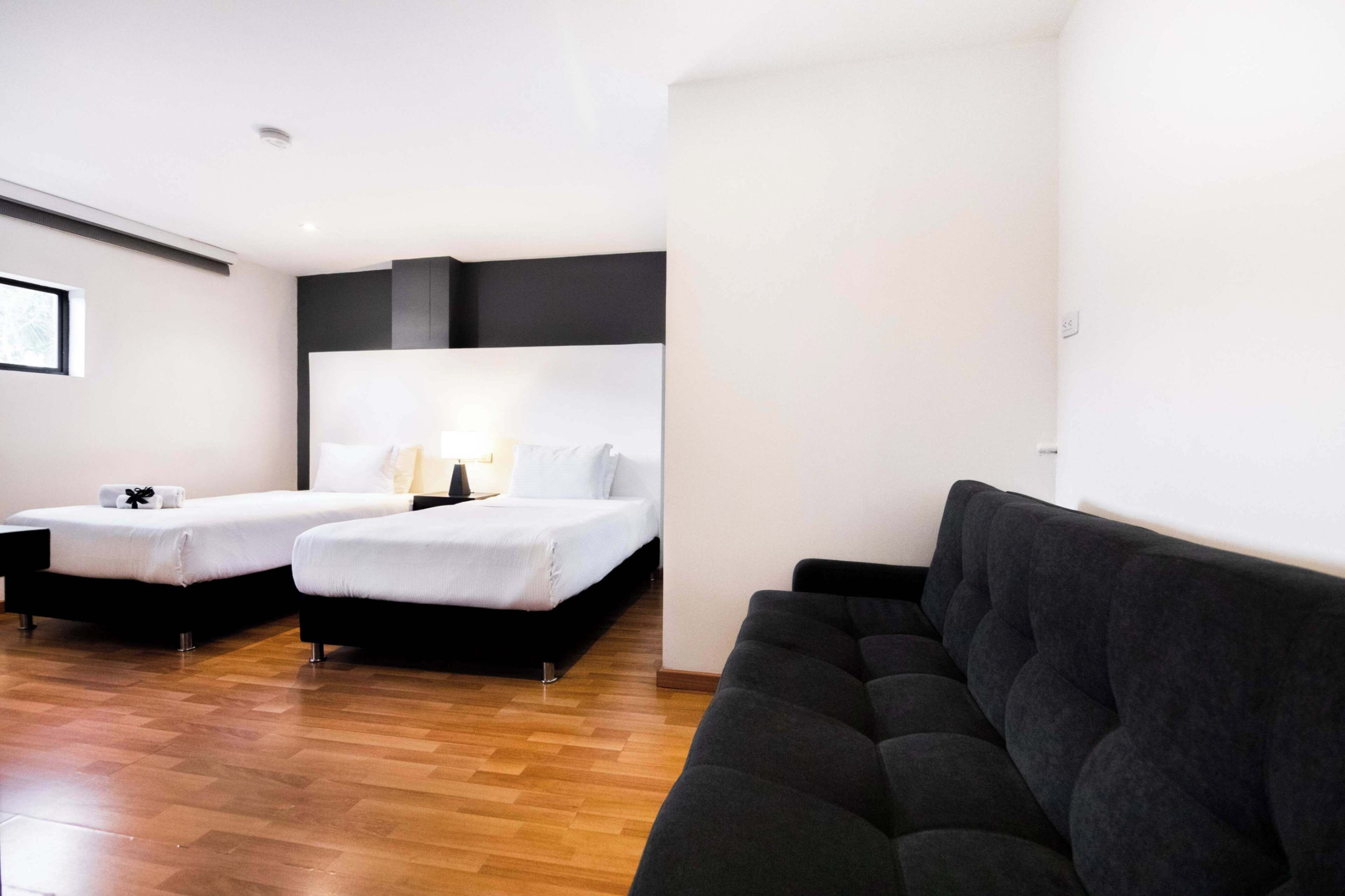A hotel room with two single beds, a dark sofa, and a wooden floor.