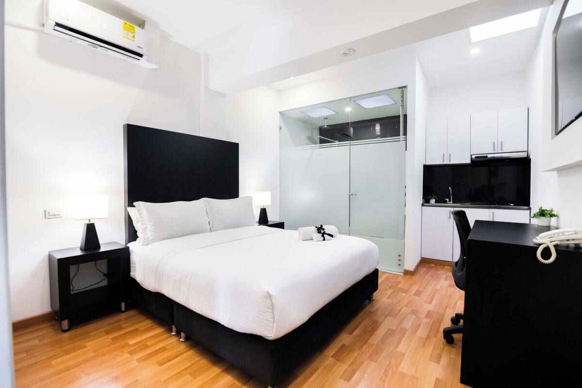 A modern hotel room with a large bed, a desk, a wardrobe, and a TV.