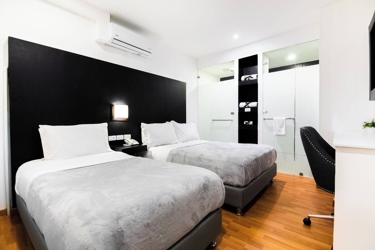 A modern hotel room with two beds, a desk, a chair, and a walk-in closet.