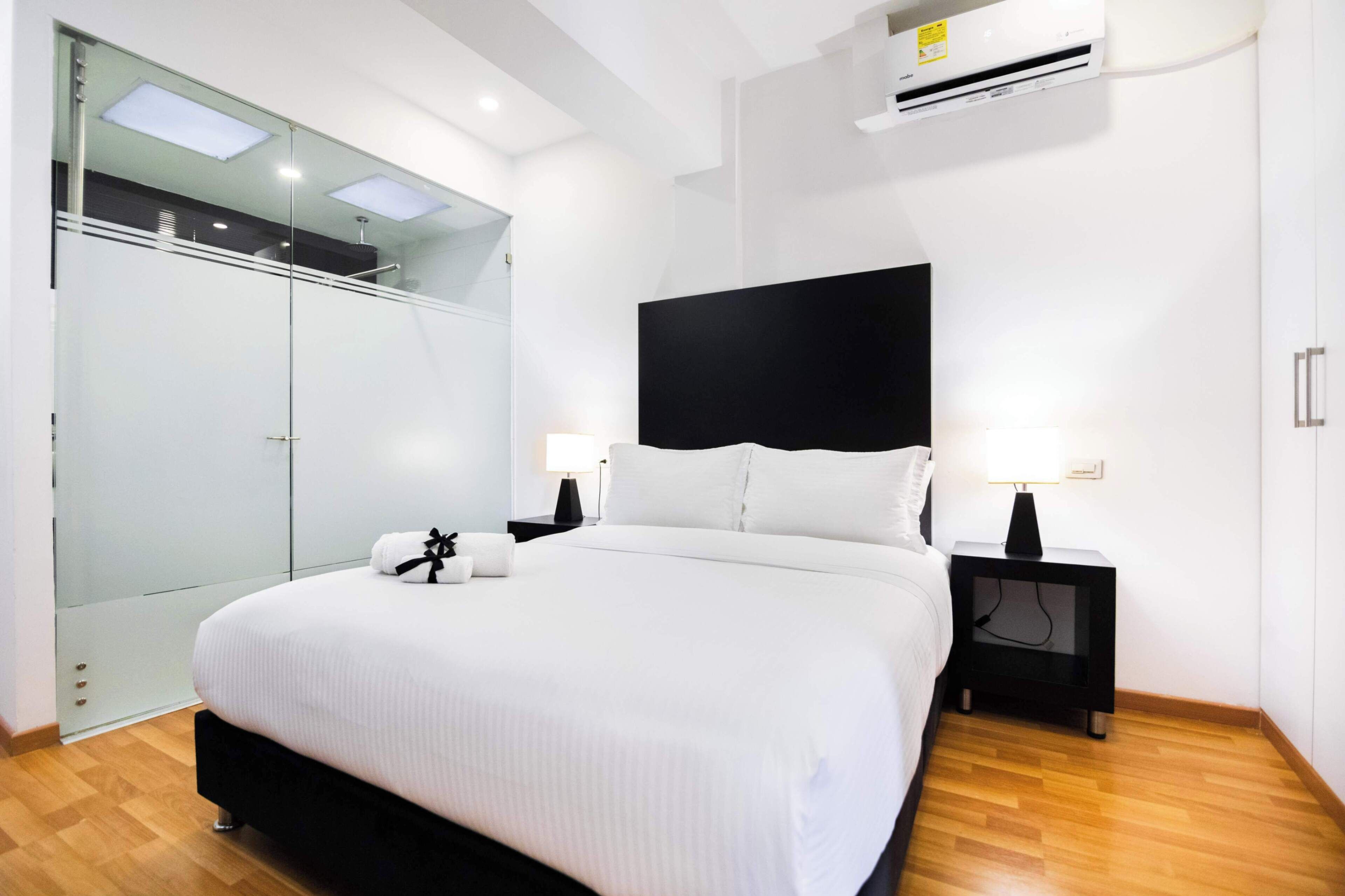Ein modernes Schlafzimmer mit einem großen Bett, einem Glastisch und einem schwarzen Kopfteil.