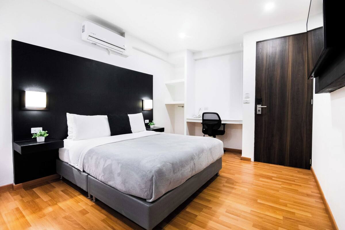 A modern bedroom with a large bed, a desk, and a wardrobe.