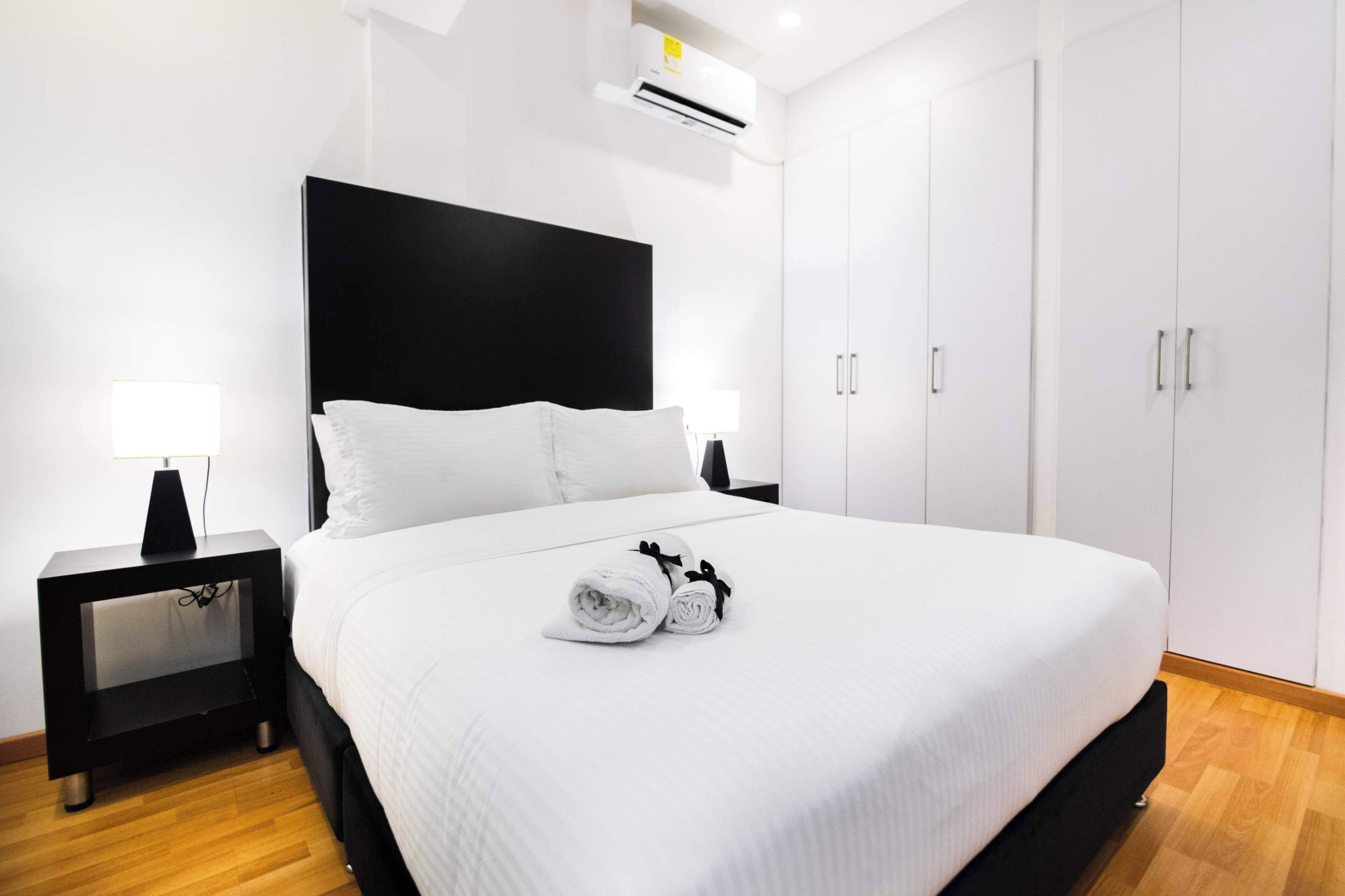 Een moderne hotelkamer met een groot bed, witte lakens, een zwart hoofdbord, een nachtkastje met een lamp en een garderobe.