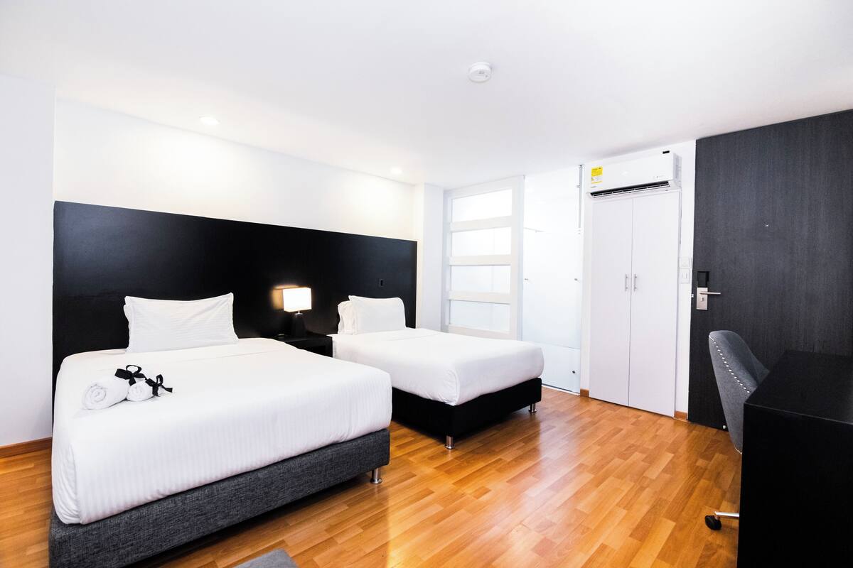 A hotel room with two beds, a desk, a chair, a wardrobe, and a window.