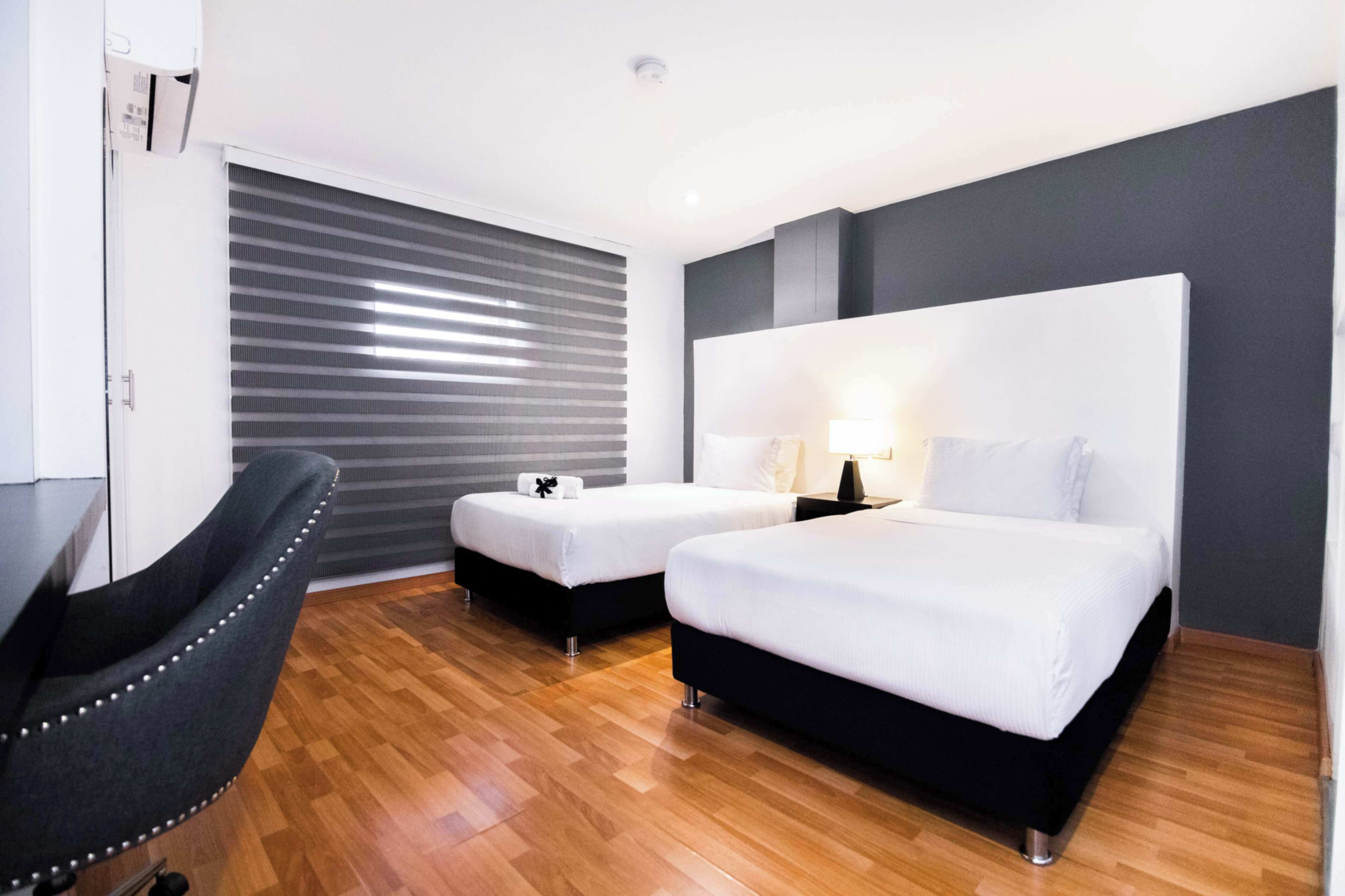 A hotel room with two beds, a desk, a chair, and a window with blinds.