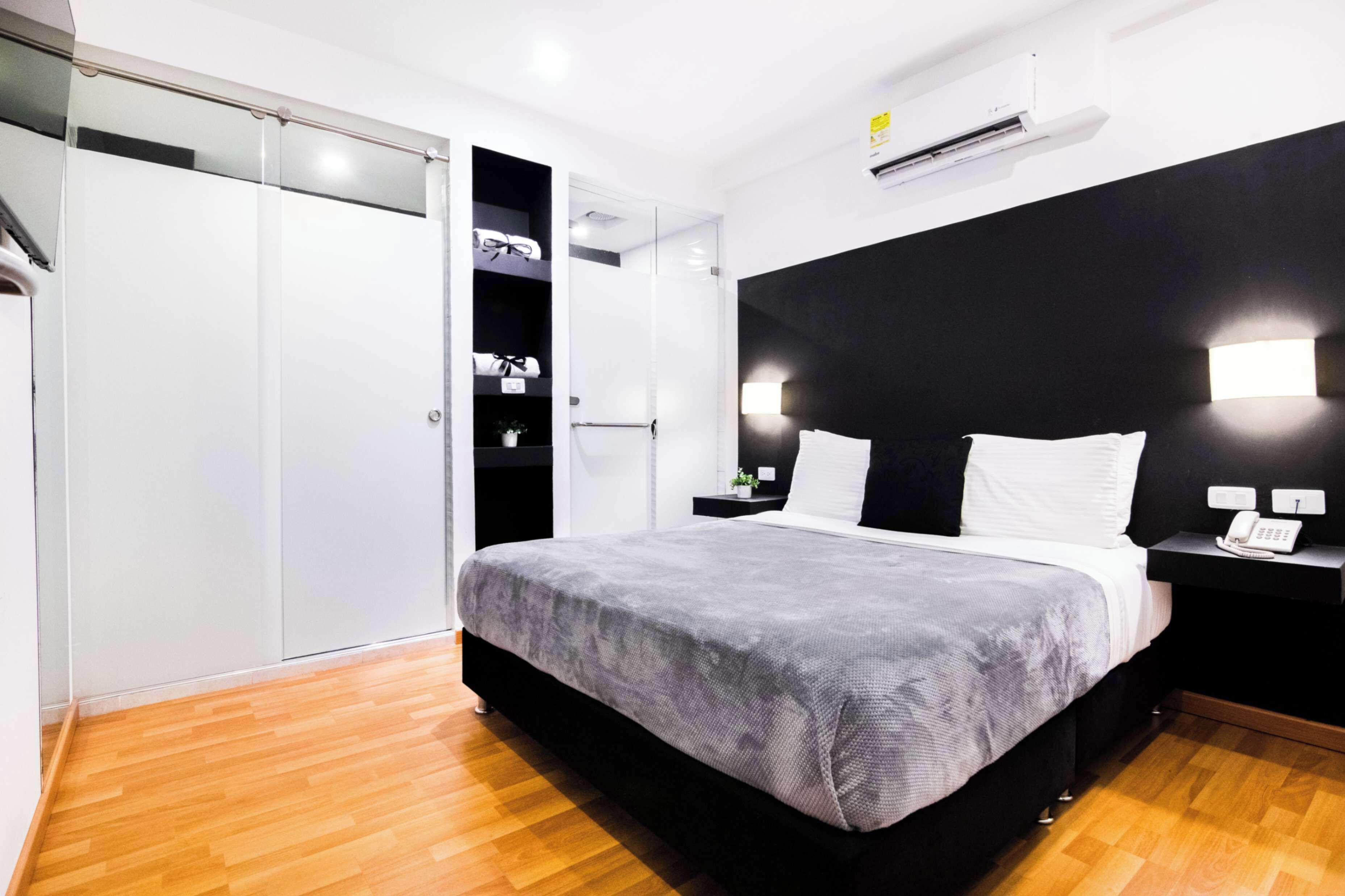 A modern hotel room with a bed, bedside tables, a wardrobe, and an air conditioning unit.