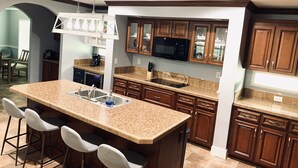 Una cocina con una isla grande, taburetes de bar, armarios de madera, un microondas y un cartel que dice "Farm Fresh".